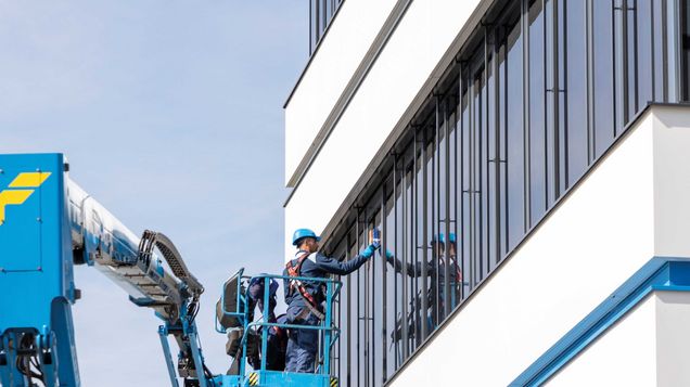 Arbeiter auf Arbeitsbühne tragen eine PSAgA beim Reinigen der Fenster der Felbermayr Zentrale in Wels. 