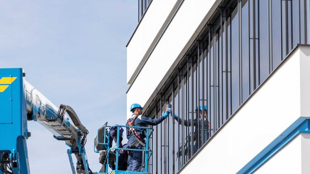 Arbeiter auf Arbeitsbühne tragen eine PSAgA beim Reinigen der Fenster der Felbermayr Zentrale in Wels. 