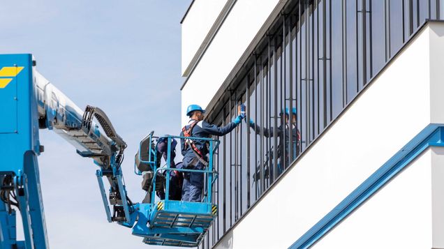 Arbeiter auf Arbeitsbühne tragen eine PSAgA beim Reinigen der Fenster der Felbermayr Zentrale in Wels. 